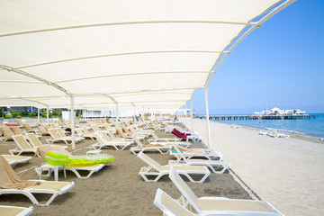 White plastic sunbeds in sandy beach under big parasol