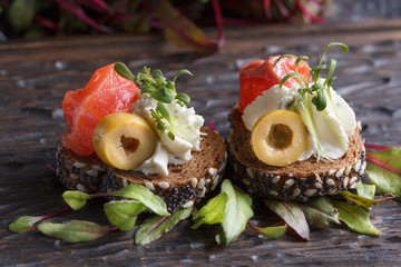 Delicious canape with salmon, cottage cheese, olive with micro greens on a dark background. Cold...