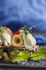 Delicious canape with salmon, cottage cheese, olive with micro greens on a dark background. Cold...