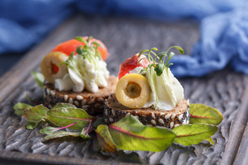 Delicious canape with salmon, cottage cheese, olive with micro greens on a dark background. Cold appetizer.