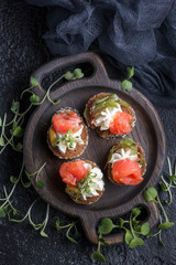 Delicious canape with salmon, cottage cheese, olive with micro greens on a dark background. Cold...