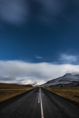Starry night and empty driving road in Iceland with snowy mountains on the background