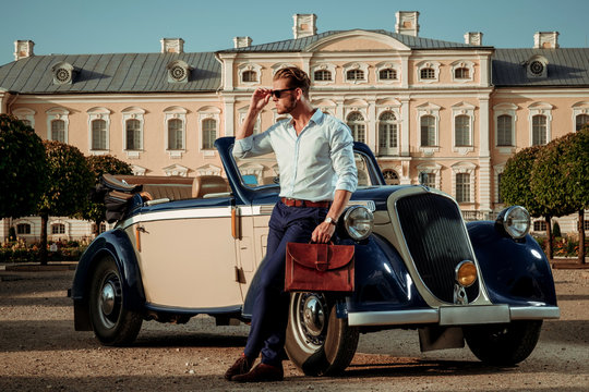 Confident wealthy young man with briefcase near classic convertible