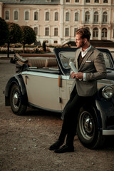 Confident wealthy young man with newspaper near classic convertible