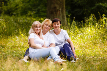 Fototapeta premium Happy mother and two adult daughters sitting in the park on the grass