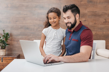 happy father and daughter using laptop while sitting at table at home