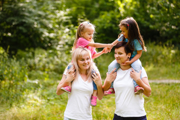 Fototapeta premium Two women are walking with children on their shoulders in the park.