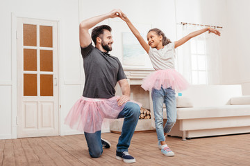 multicultural father and daughter in pink tutu tulle skirts dancing at home