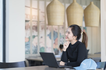 Young asian beautiful woman thinking looking to the side at copy space. Woman working with laptop at coffee shop workplace.