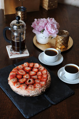 Strawberry cheesecake, coffee in French press, white cups, pink peonies in a funny vase, golden candlestick on a tray