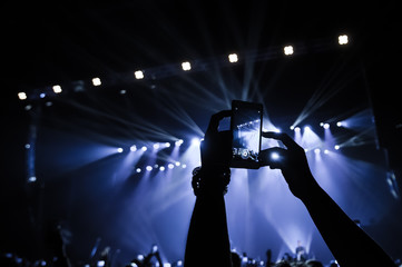 People in the crowd at a concert make video recordings and pics on a smartphone of published in...