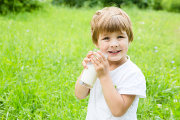Smiling little boy drink milk on the green meadow.