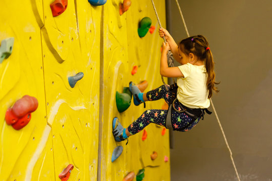 little girl climbing a rock wall indoor