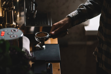 The process of making coffee step by step. Barista man holding a portafilter with freshly ground coffee beans in it, preparing for tamping.