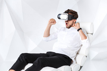 Excited young man is getting experience using VR-headset glasses of virtual reality gesticulating...