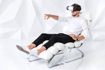 Excited young man is getting experience using VR-headset glasses of virtual reality gesticulating...