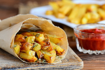 Crunchy fried potatoes with spices. Spicy fried potatoes in paper, ketchup sauce. A wooden background. Quick potato recipe. Closeup