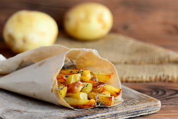 Fried potatoes with spices. Homemade fried potatoes in paper and on a wooden table. Potato snack recipe. Country style