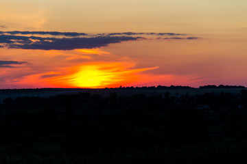 Orange sunset over silhouettes of village and trees