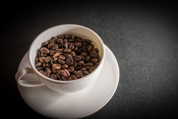 Roasted coffee beans in white cup on dark background. Selective focus.
