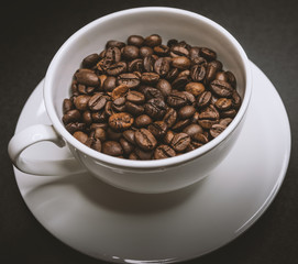 Roasted coffee beans in white cup on dark background. Selective focus.
