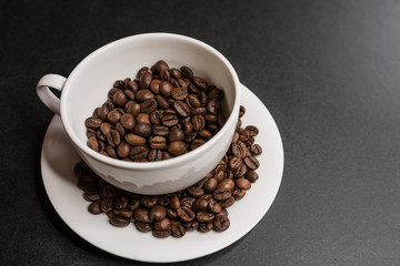 Roasted coffee beans in white cup on dark background. Selective focus.