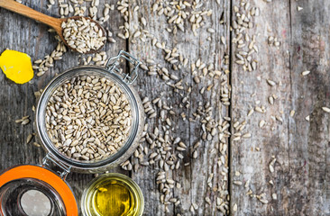 Glass of oil from sunflower seeds in rustic jar on wooden table, flat lay from above