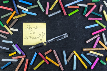 Back to school text, note on card on blackboard black background, reminder about start of education