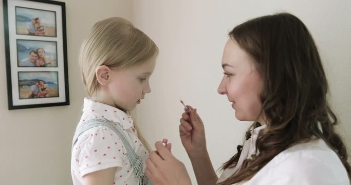 Mother makes up daughter's lips with lipstick at home.