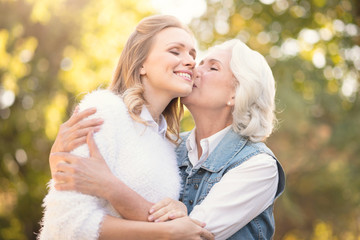 Fototapeta premium Aging mother kissing loving daughter in the park