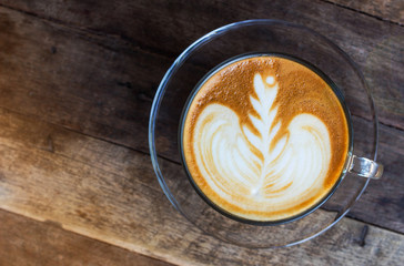 Small flower design of latte art coffee in clear cup on old wooden table , warm light