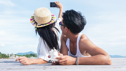 Young couple of lover laying down on the wooden floor near the beach taking themselves a photo