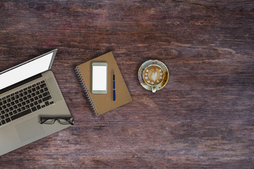 Top view of office desktop, laptop,smart phone and cup of coffee on wood table.	