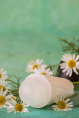 Fototapeta na wymiar Daily body care and hygiene. Roller deodorant and fresh chamomile flowers on a green background. For gentle and sensitive skin.