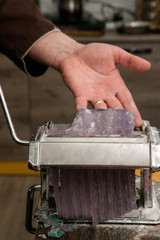 Chief with pasta machine does violet dough for noodles on wooden table. Top view colourful food concept