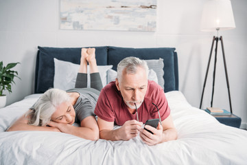 man using smartphone while wife sleeping near by in bed
