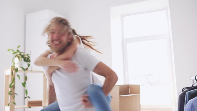 Cool Caucasian pair having fun in their new apartment and rejoicing in slowmotion. Concpet of happines and joy