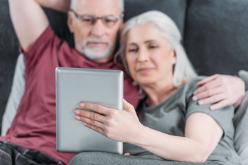 Fototapeta premium selective focus of senior couple with digital tablet resting in bed together