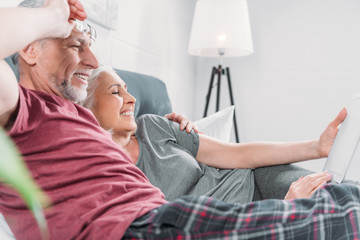 happy senior couple with digital tablet resting in bed together