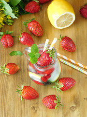 Refreshing soft drink with ice cubes, strawberries and mint surrounded by fresh strawberries on a wooden background. View from above