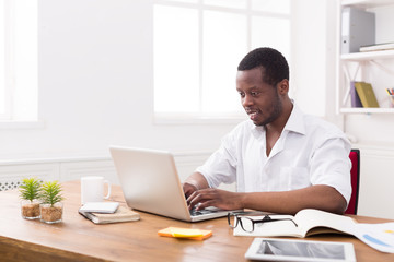 Fototapeta premium Black happy businessman in white office, work with laptop