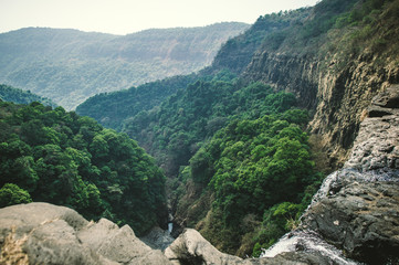 View from a cliff with a waterfall on a green valley and mountains in India