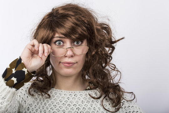 Ritratto di Donna con capelli lunghi  e voluminosi e maglione chiaro che guarda si tiene gli occhiali con aria stupita e smarrita - sfondo bianco