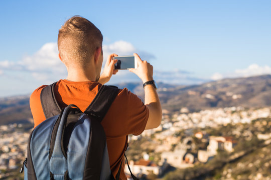 Travel, vacation, photographer and hitchhiker concept - raveler man photographed mountains and city in the smartphone