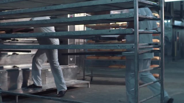 The male workers of baking factory in white uniforms put the bread dough to be baked in the large oven. Machinery production, business. Modern technologies, tasty bread. Pastry industry.