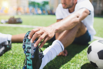 selective focus of soccer player holding football boot while sitting on pitch