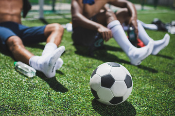 soccer players resting on football field with soccer ball on foreground