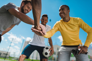 Low angle view of happy multiethnic soccer team holding hands together before game