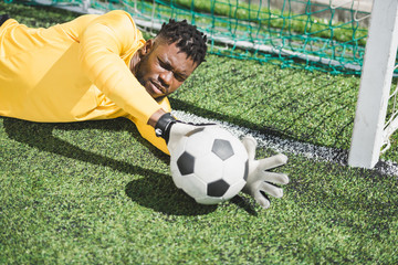 portrait of african american goalkeeper catching ball during soccer match