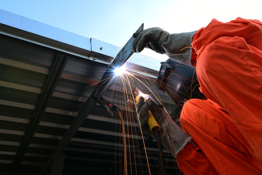 Industrial worker welding at factory and many sharp sparks steel welder on roof, high angle view .